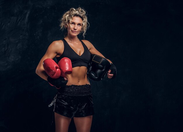Ervaren vrouwelijke bokser poseert voor fotograaf in donkere fotostudio met apparatuur in haar handen.