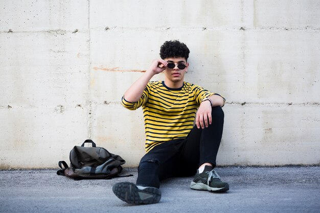 Etnische jonge man met coole kapsel zittend op asfalt
