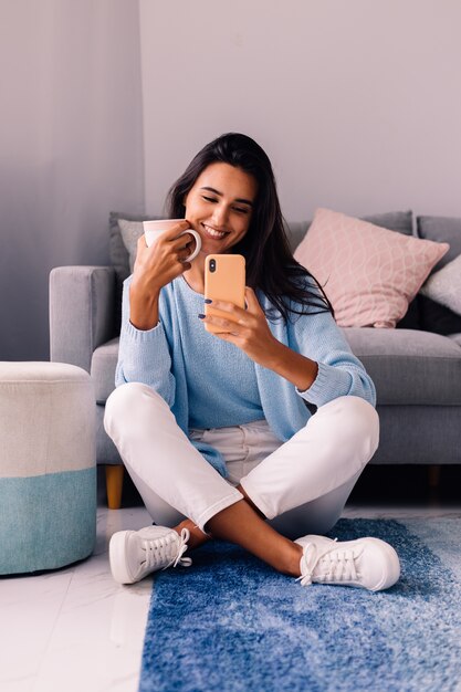 Europese fit brunette fashion blogger vrouw zit op de vloer in de woonkamer in de buurt van de bank