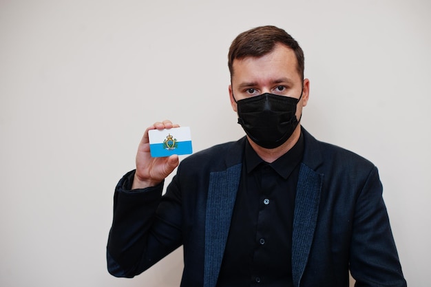Europese man draagt zwart formeel en beschermt gezichtsmasker houdt San Marino-vlagkaart geïsoleerd op witte achtergrond Europa coronavirus Covid-landconcept