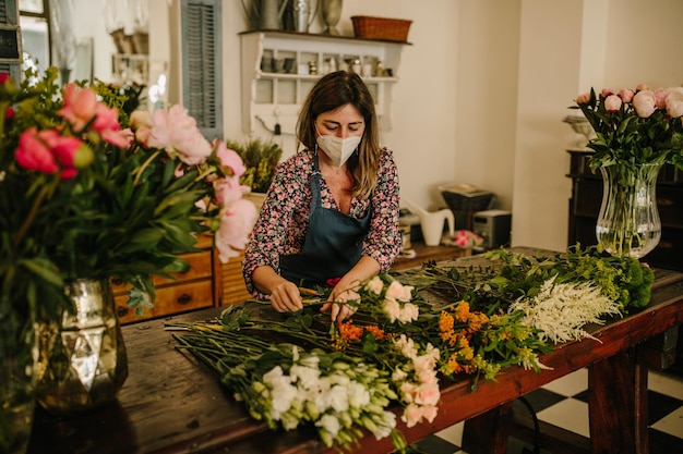 Europese vrouwelijke bloemist met een medisch gezichtsmasker die bloemstukken maakt in bloemontwerpstudio