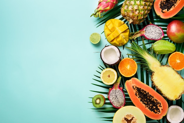 Exotisch fruit en tropische palmbladeren - papaja, mango, ananas, banaan, carambola, drakenfruit, kiwi, citroen, sinaasappel, meloen, kokosnoot, limoen.