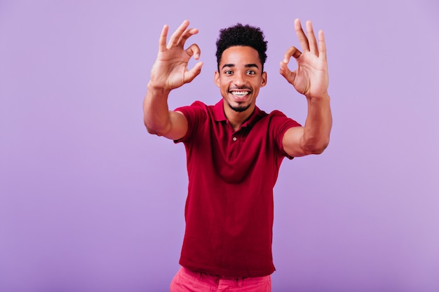 Extatische jongeman die positieve emoties op violette muur uitdrukt. foto van lachende nieuwsgierige man met donker haar.