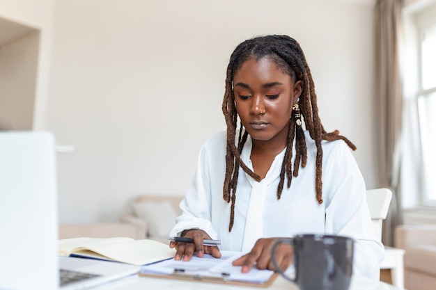 Externe baantechnologie en mensenconcept gelukkig lachende jonge zwarte zakenvrouw met laptopcomputer en papieren die thuis werken