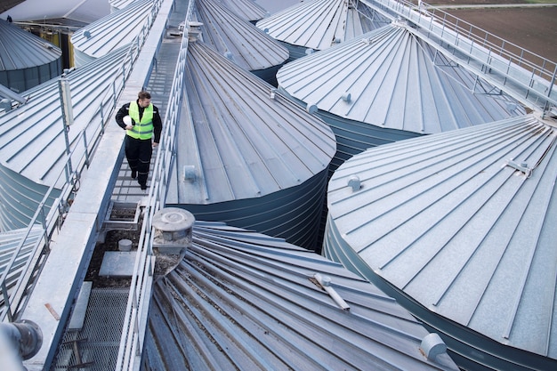 Fabrieksarbeider die op metalen platform loopt en visuele inspectie doet op industriële voedselopslagtanks of silo's