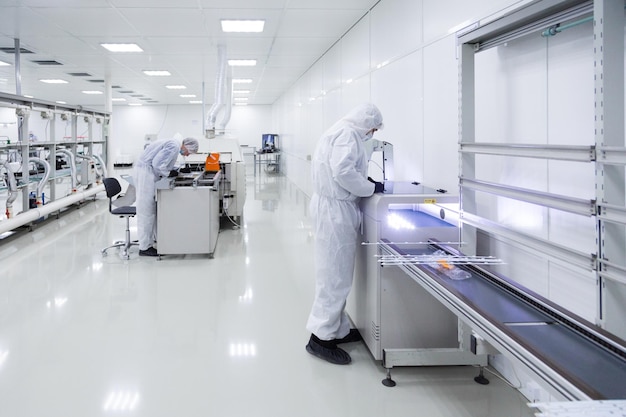 Fabrieksarbeiders in witte laboratoriumpakken en zwarte latexhandschoenen werken met moderne apparatuur in een zeer schone kamer