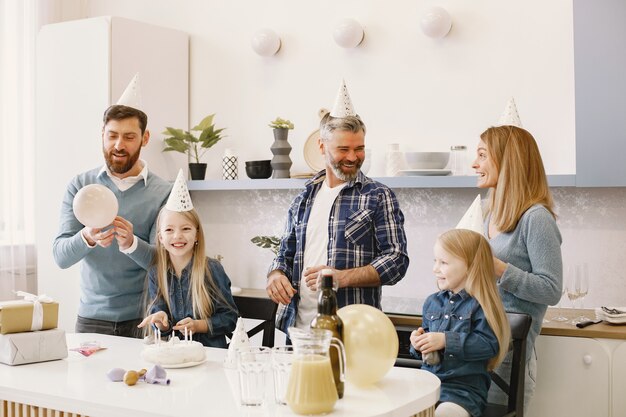 Familie en twee van hun dochters vieren feest. Mensen die een ballon blazen. Cadeautjes staan op tafel.