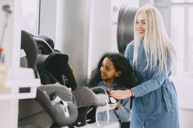 Familie in een autosalon. Vrouw die de autostoel koopt. Weinig Afrikaans meisje met mther.