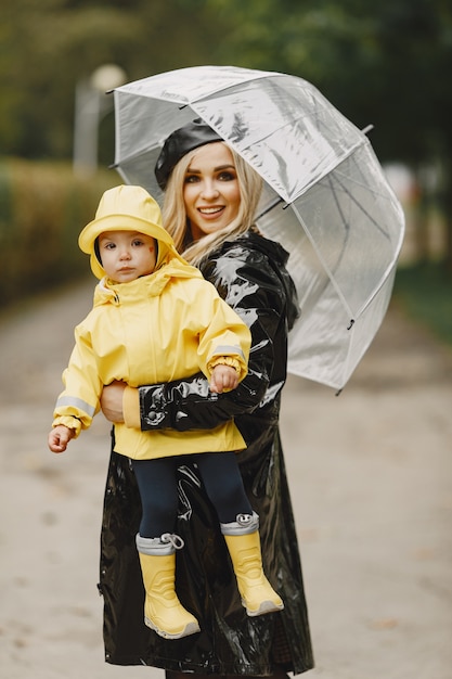 Familie in een regenachtig park. Kid in een gele regenjassen en vrouw in een zwarte jas.