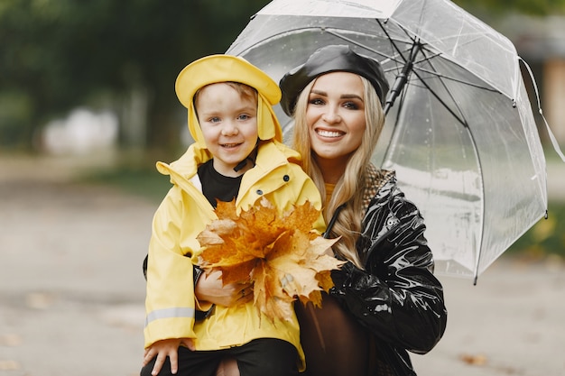 Familie in een regenachtig park. Kid in een gele regenjassen en vrouw in een zwarte jas.