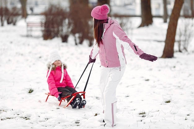 Familie in gebreide wintermutsen op familiekerstvakantie. Vrouw en meisje in een park. Mensen spelen met slee.