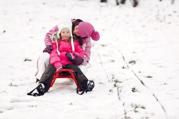 Familie in gebreide wintermutsen op familiekerstvakantie. Vrouw en meisje in een park. Mensen spelen met slee.