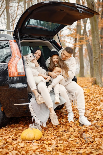 Familie rust na een dag buiten doorbrengen in het herfstpark Vader moeder hun dochter en hond zitten in de kofferbak glimlachend Familie dragen beige sportieve kostuums