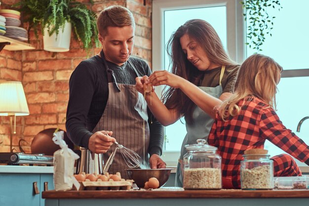 Familieconcept. Moeder vader en dochtertje samen koken ontbijt in loft-stijl keuken.