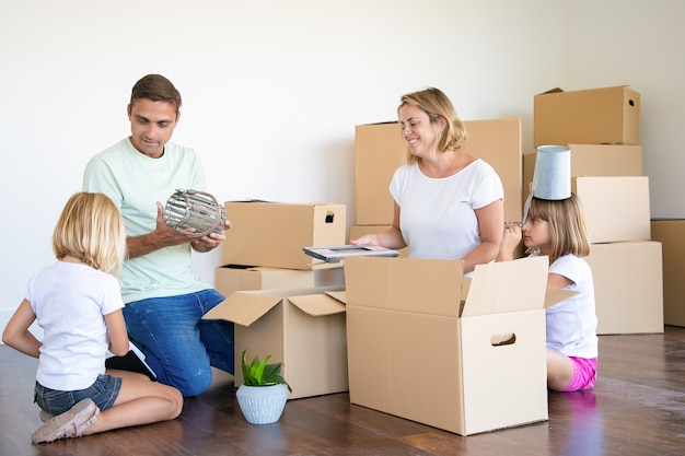 Gratis foto familiepaar en kleine meisjes verhuizen naar een nieuwe flat, plezier hebben terwijl ze dingen uitpakken in een nieuw appartement, op de vloer zitten en objecten uit open dozen halen