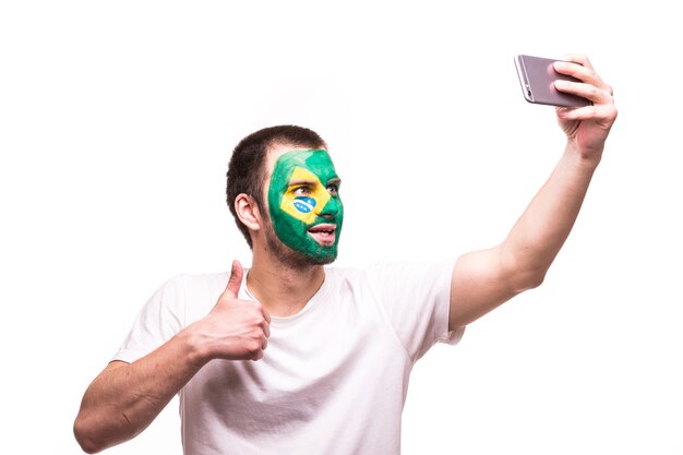 Fanondersteuning van het Braziliaanse nationale team neemt selfie aan de telefoon met geverfd gezicht geïsoleerd op een witte achtergrond