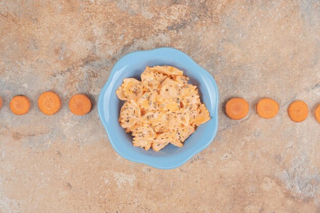 Farfalle met kaassaus en wortelplakken op oranje ruimte.