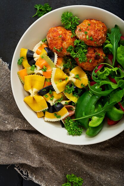 Farfalle pasta harde tarwe met gebakken gehaktballetjes van kipfilet in tomatensaus en salade in kom.