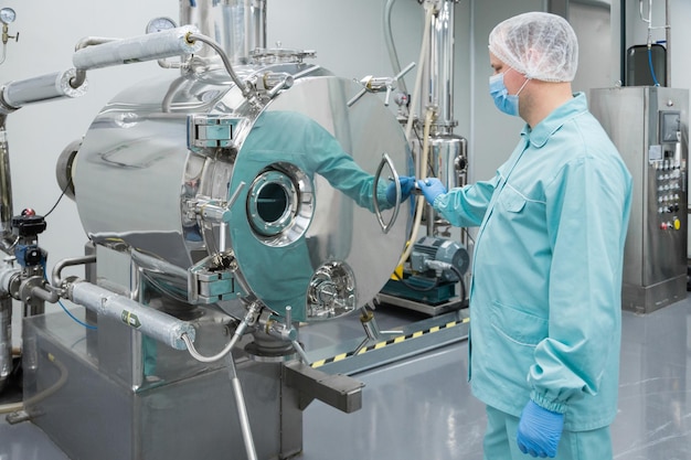 Farmaceutische fabrieksarbeider in beschermende kleding die aan apparatuur werkt in steriele werkomstandigheden