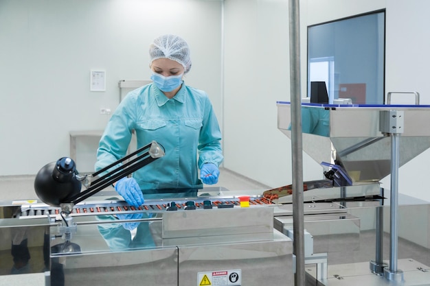 Farmaceutische industrie vrouw werknemer in beschermende kleding werkende productie van tabletten in steriele arbeidsomstandigheden