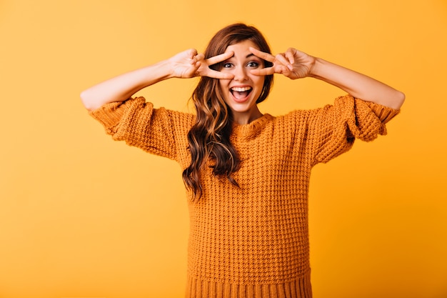 Fascinerende blanke vrouw die gekke bekken trekt en lacht. Studio portret van spectaculair meisje draagt gebreide oranje kledij.