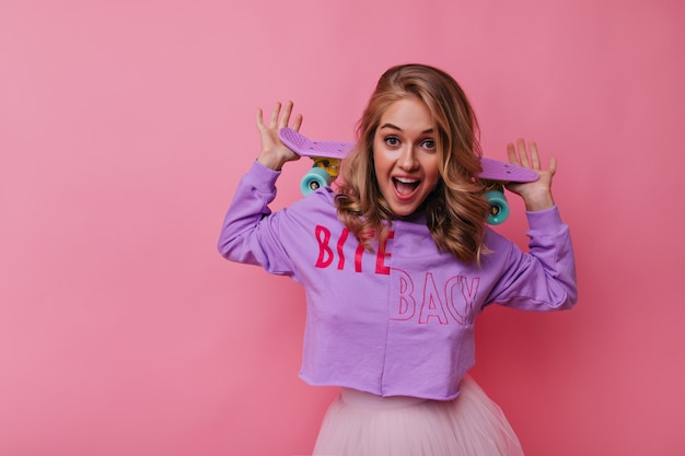 Fascinerende blanke vrouw in trendy shirt met roze skateboard. Leuk blonde vrouwelijk model dat van vrije tijd geniet.