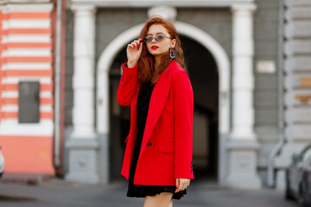 fashion model demonstreren trendy slijtage en accessoires. Casual rood jasje, zwarte korte jurk.