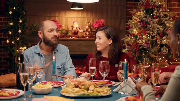 Feestelijk paar dat Kerstmis viert aan de eettafel met naaste familieleden. Positieve mensen zitten in de woonkamer om authentieke traditionele wintervakantie te vieren met dierbaren.