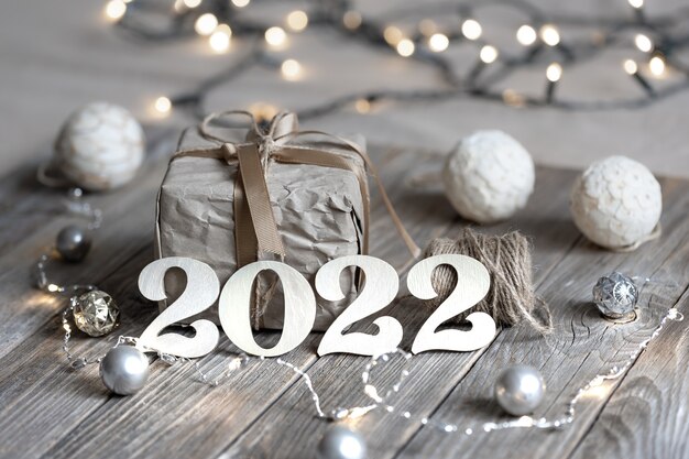 Feestelijke kerstcompositie met houten nummers 2022, geschenkdoos en kerstballen op onscherpe achtergrond met bokeh.