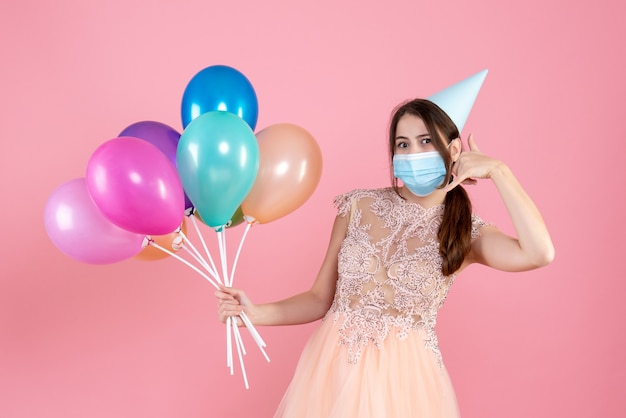 feestmeisje met feestmuts met kleurrijke ballonnen bel me telefoongebaar op roze