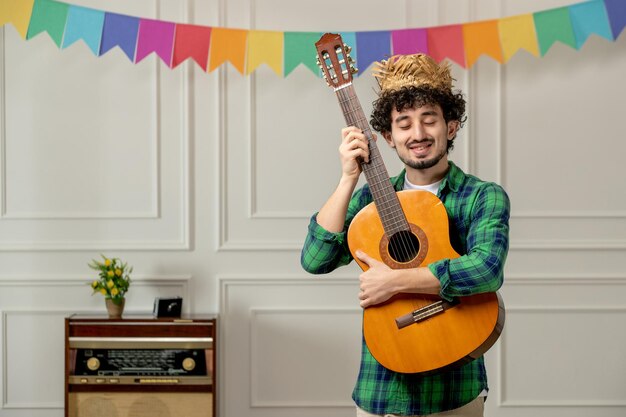 Festa junina schattige jonge kerel in strohoed met retro radio en kleurrijke vlaggen met gitaar