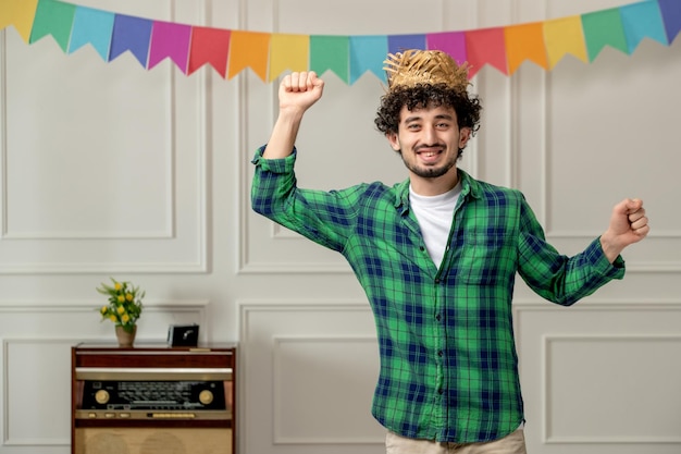 Festa junina schattige jonge kerel in strohoed met retro radio en vlaggen die vrolijk dansen