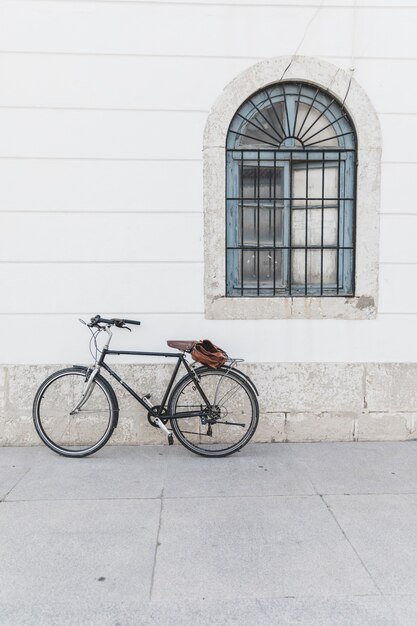 Fiets die op witte muur met venster wordt geparkeerd