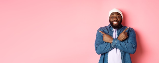 Fijne jonge Afro-Amerikaanse hipster-kerel die met de vingers zijwaarts glimlacht en twee keuzemogelijkheden toont