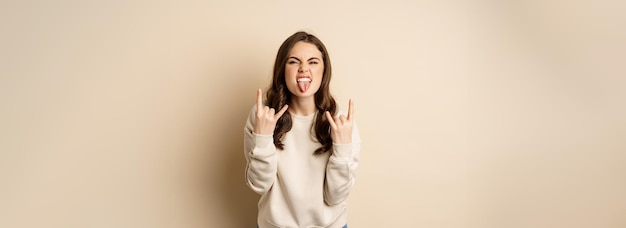 Gratis foto fijne jonge vrouw die geniet van muziek die plezier heeft met het tonen van rock op heavy metal vingerhoorns gebaar standin