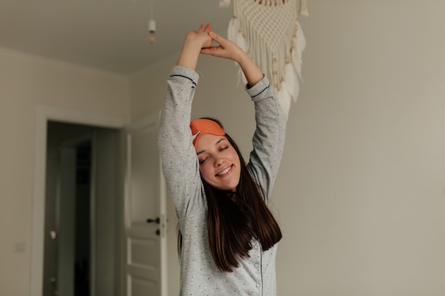 Fijne ochtend thuis. Jonge mooie vrouw met donker haar, gekleed in een slaapmasker dat zich uitstrekt door de troon op het bed.