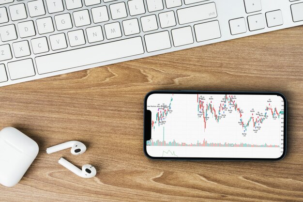 Financiële beursgrafiek op het smartphonescherm op houten achtergrond met een computer ernaast. bovenaanzicht. beurs.
