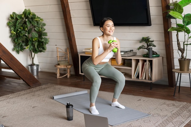 Fit en gezonde Aziatische vrouw doet squats thuis workout fitness trainingssessie met halters en...