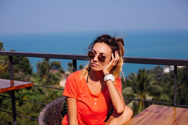 Fit gelooide getatoeëerde blanke Europese vrouw met sportlichaam en buikspieren, in korte broek en rood oranje shirt