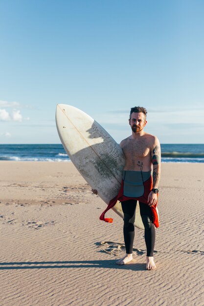 Fit man van middelbare leeftijd met surfplank op leeg strand op warme zomerdag