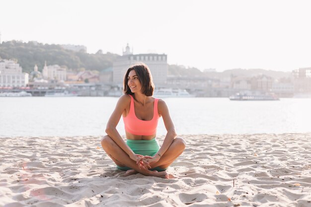 Fit sportieve vrouw in perfecte vorm bij zonsondergang op het strand in yoga pose kalm