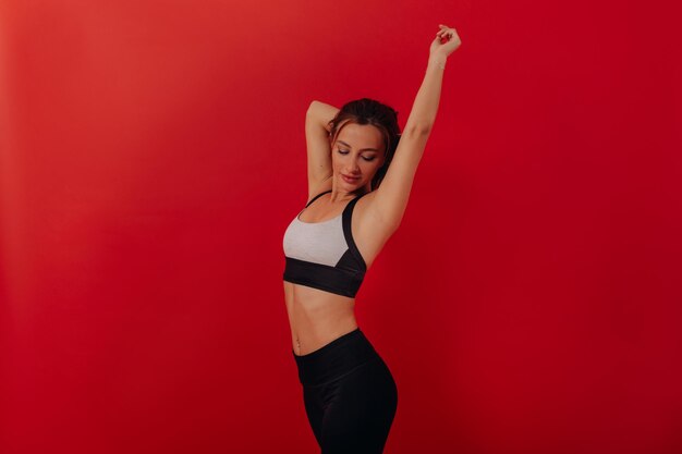 Fit stijlvolle vrouw in sport top en broek doet stretching over rode achtergrond