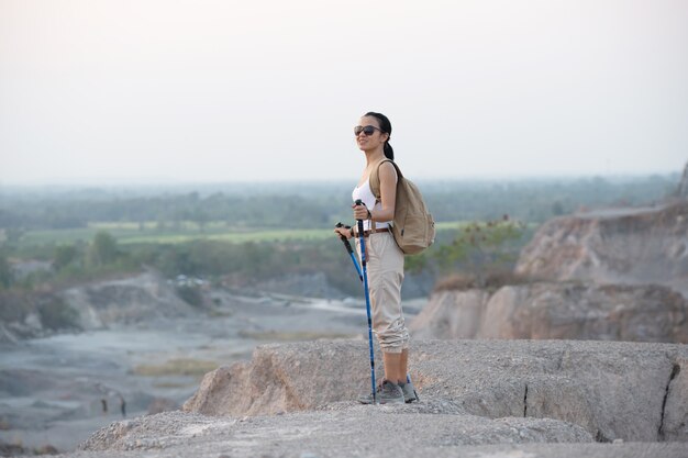 Fit vrouwelijke wandelaar met rugzak en stokken staande op rotsachtige bergkam uitkijkend op valleien en piek.