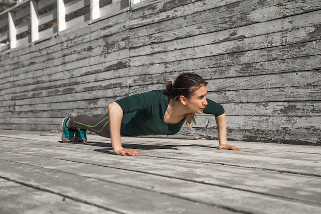 fitness sportieve meisje in sportieve kleding doet oefeningen op een houten achtergrond, lichte achtergrond, het concept van sport