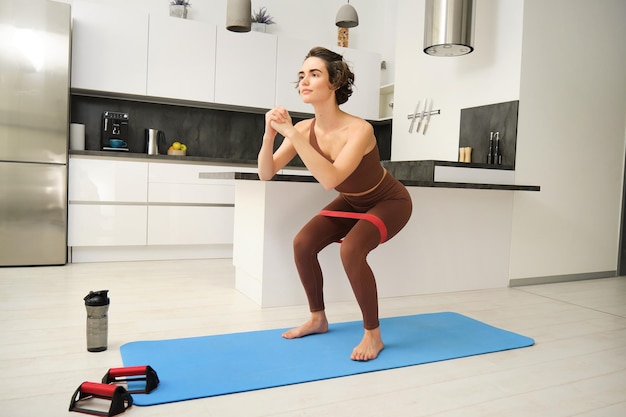 Gratis foto fitness thuis jong sportvrouwmeisje in activewear die squats doet in haar keukentraining binnenshuis
