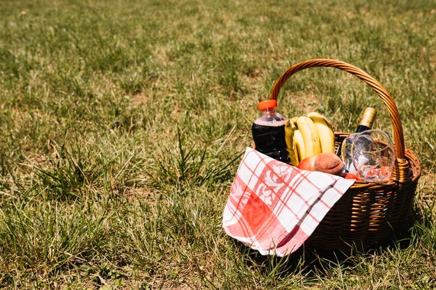 Fles champagne; wijnglazen; sapfles; fruit en servet in rieten mand op groen gras