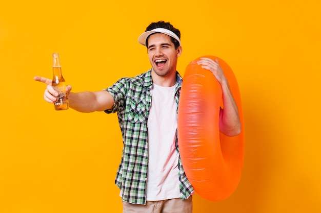 Flirterige man in goed humeur knipoogt en poseert met flesje bier en opblaasbare oranje cirkel.