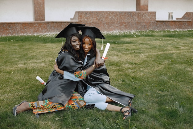 Focus op een twee jonge afro-amerikaanse vrouwelijke studenten gekleed in zwarte toga afstuderen. campus als achtergrond