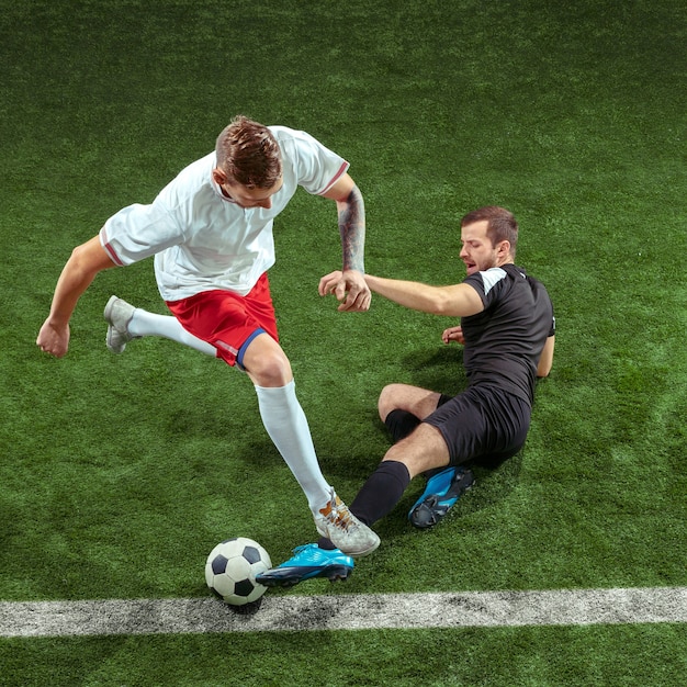 Football-speler die voor bal over groene grasmuur aanpakt. Professionele mannelijke voetballers in beweging stadium. Fit springende mannen in actie, springen, beweging in het spel.
