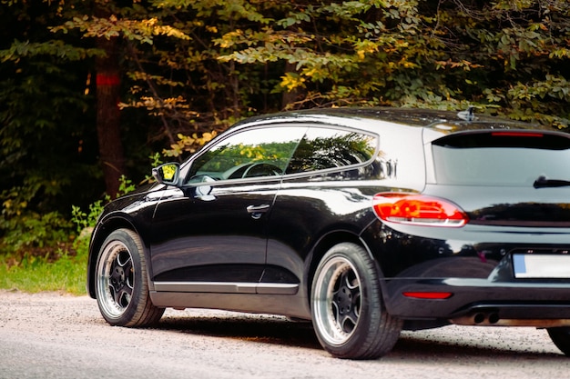 Foto aan de achterkant van een luxe zwarte glanzende auto met koele wielen die op de weg in het bos staat zonder bestuurder erin. hoge kwaliteit foto